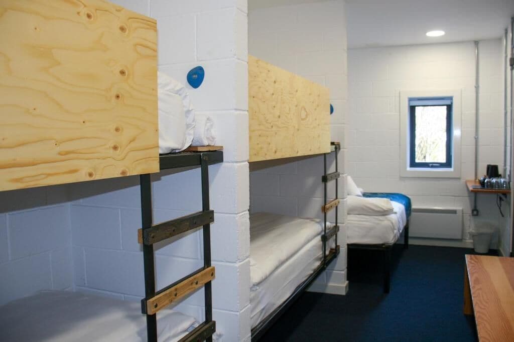 A dormitory room with bunk beds, a window, and a small desk with a chair.