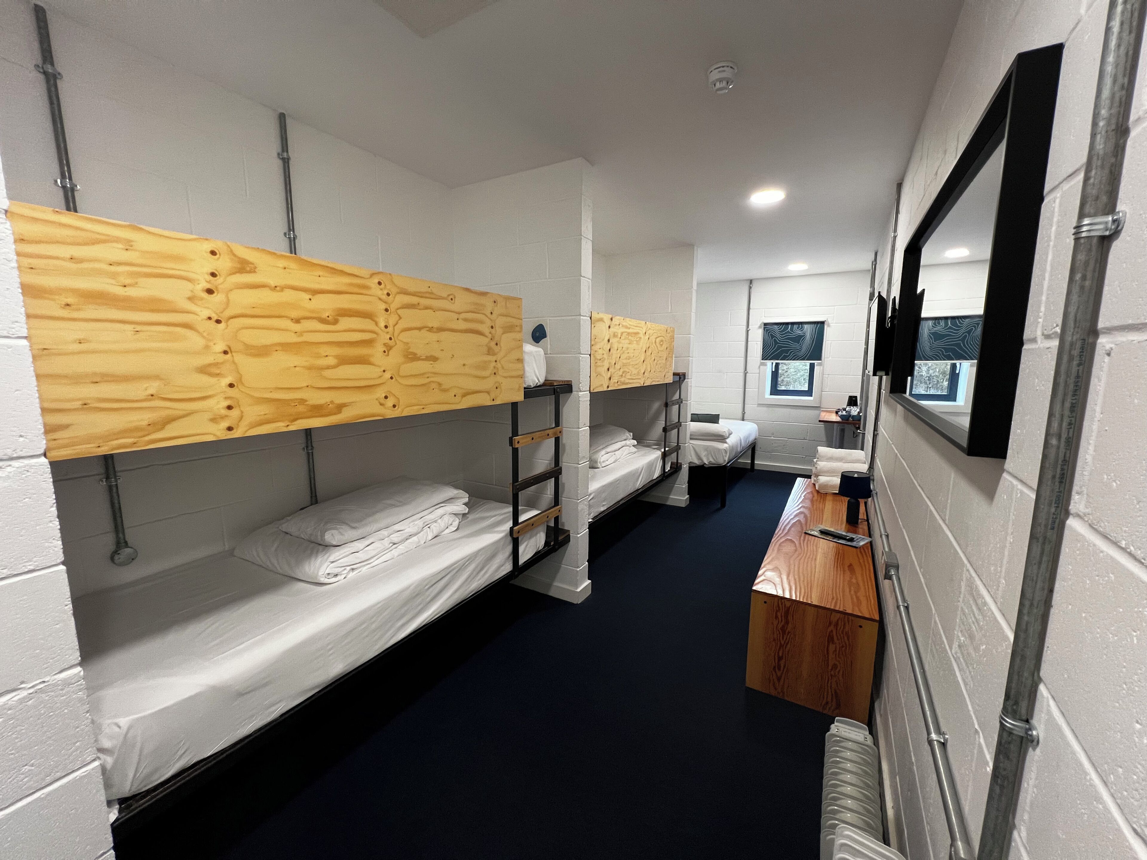 A narrow corridor with bunk beds, a wooden desk, and a window with a view.
