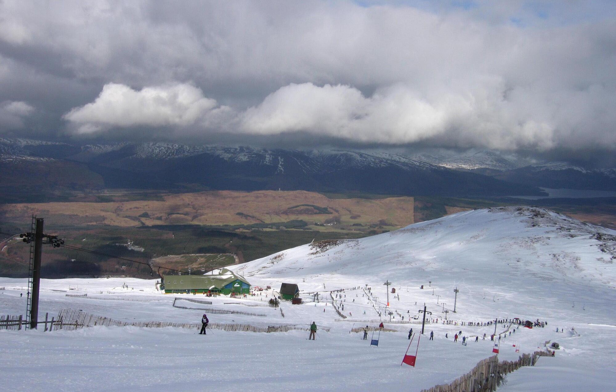 A ski resort with a chairlift, a green building, and a snowy landscape with mountains in the background.