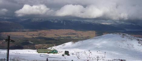 A ski resort with a chairlift, a green building, and a snowy landscape with mountains in the background.