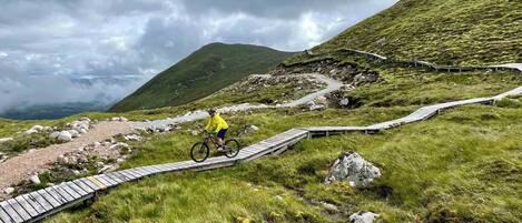 A mountain path with wooden bridges and a cyclist in a yellow jacket.