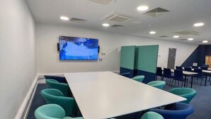 A conference room with a large table, teal chairs, a mounted TV, and a staircase in the background. - Base Camp Hotel Nevis Range (Fort William)