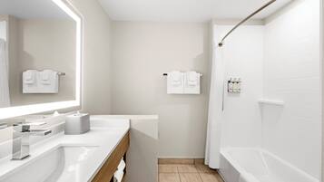 A modern bathroom with a white sink, mirror, and bathtub. There are towels hanging on the wall and a shower curtain.