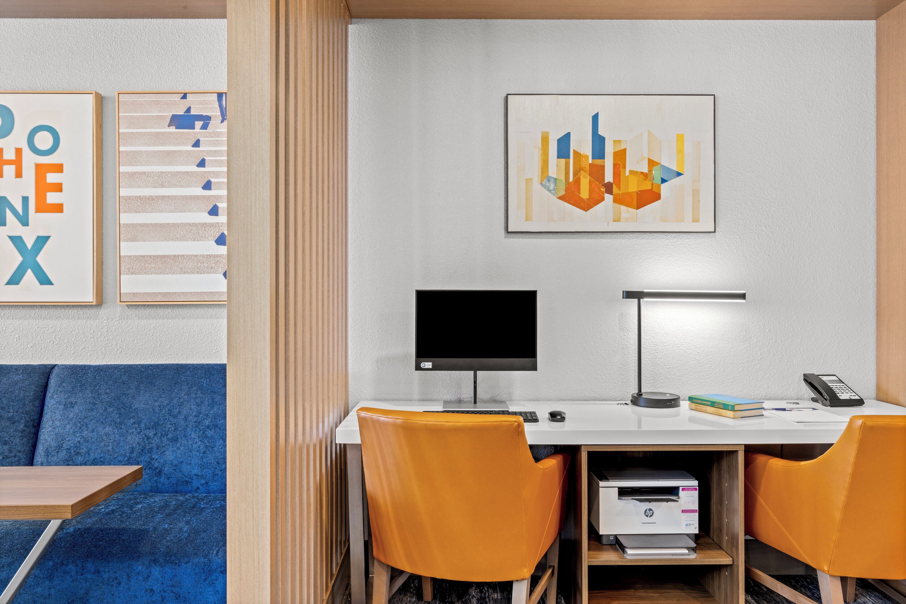 Un espacio de oficina moderno con un escritorio, dos sillas, un monitor de computadora, una impresora y obras de arte enmarcadas en la pared.