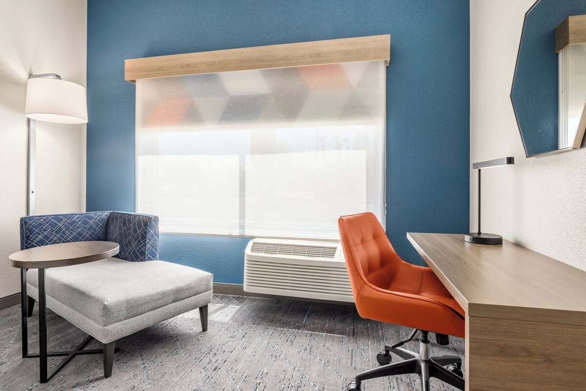 A modern room with a blue accent wall, a round table, a sofa, an orange chair, and a desk.
