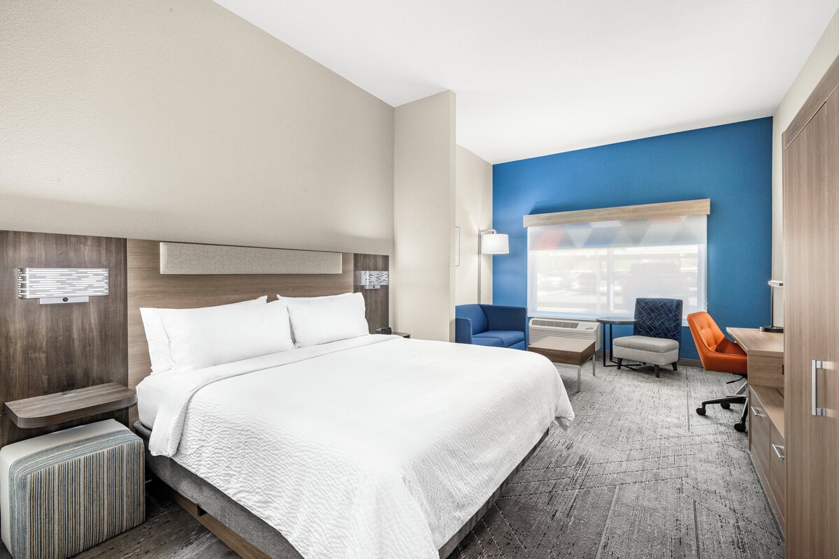 A hotel room with a large bed, a desk, a chair, and a window with a view of the parking lot.