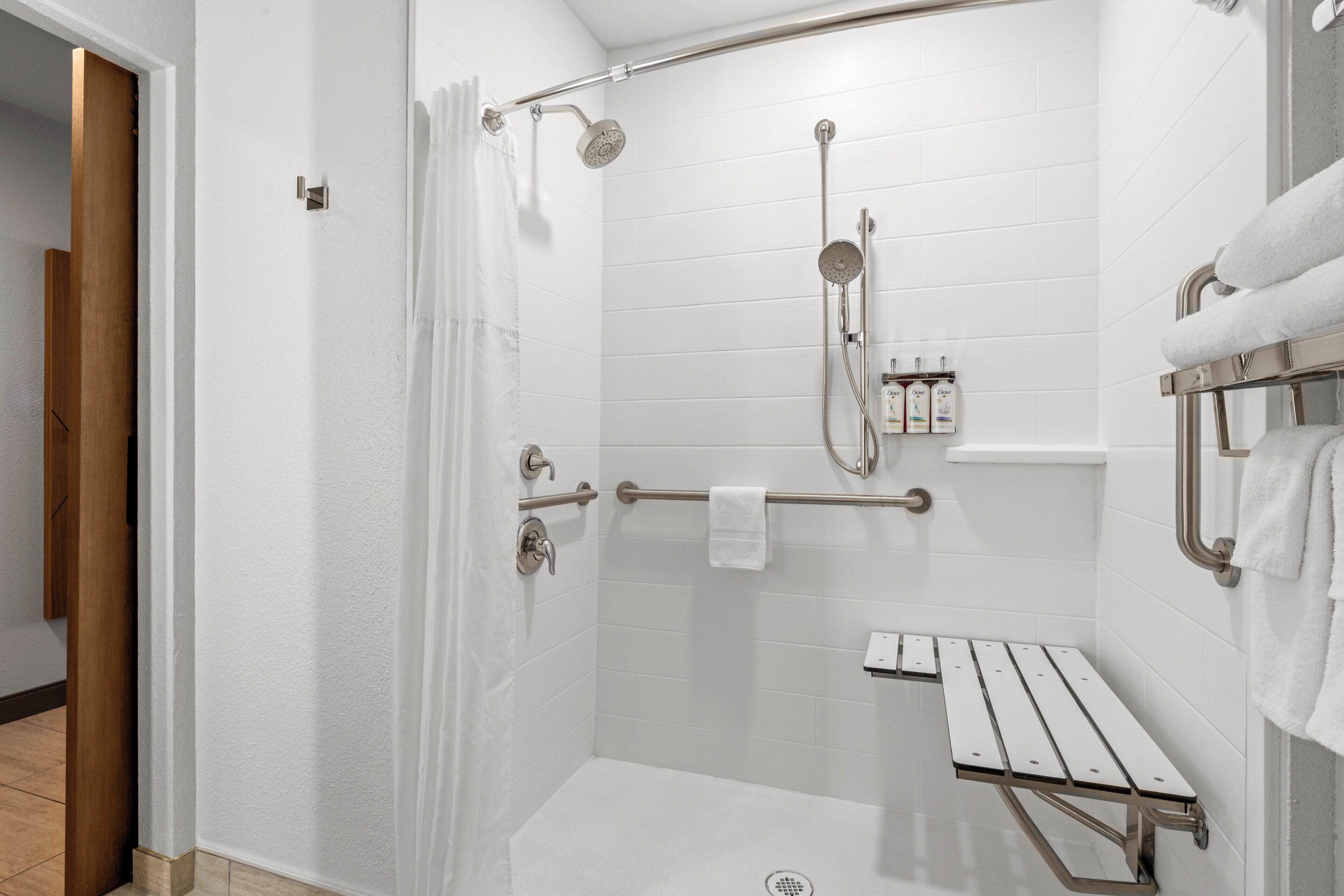 Ein modernes Duschbad mit Glasabtrennung, Handbrause, am Wand befestigtem Wasserhahn und einer kleinen Ablage für Pflegeartikel.