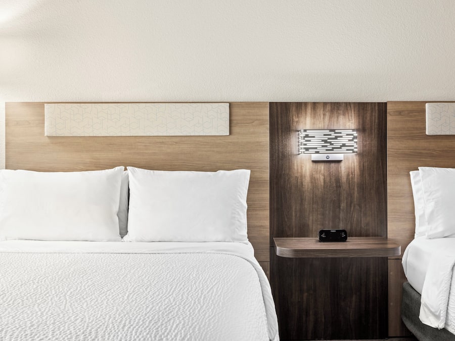 Una camera d'albergo con due letti, un comodino con una lampada e un punto luce a parete.
