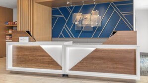 Un comptoir d’accueil d’hôtel au design moderne, avec un revêtement en bois et un mur bleu à motifs géométriques en arrière-plan.