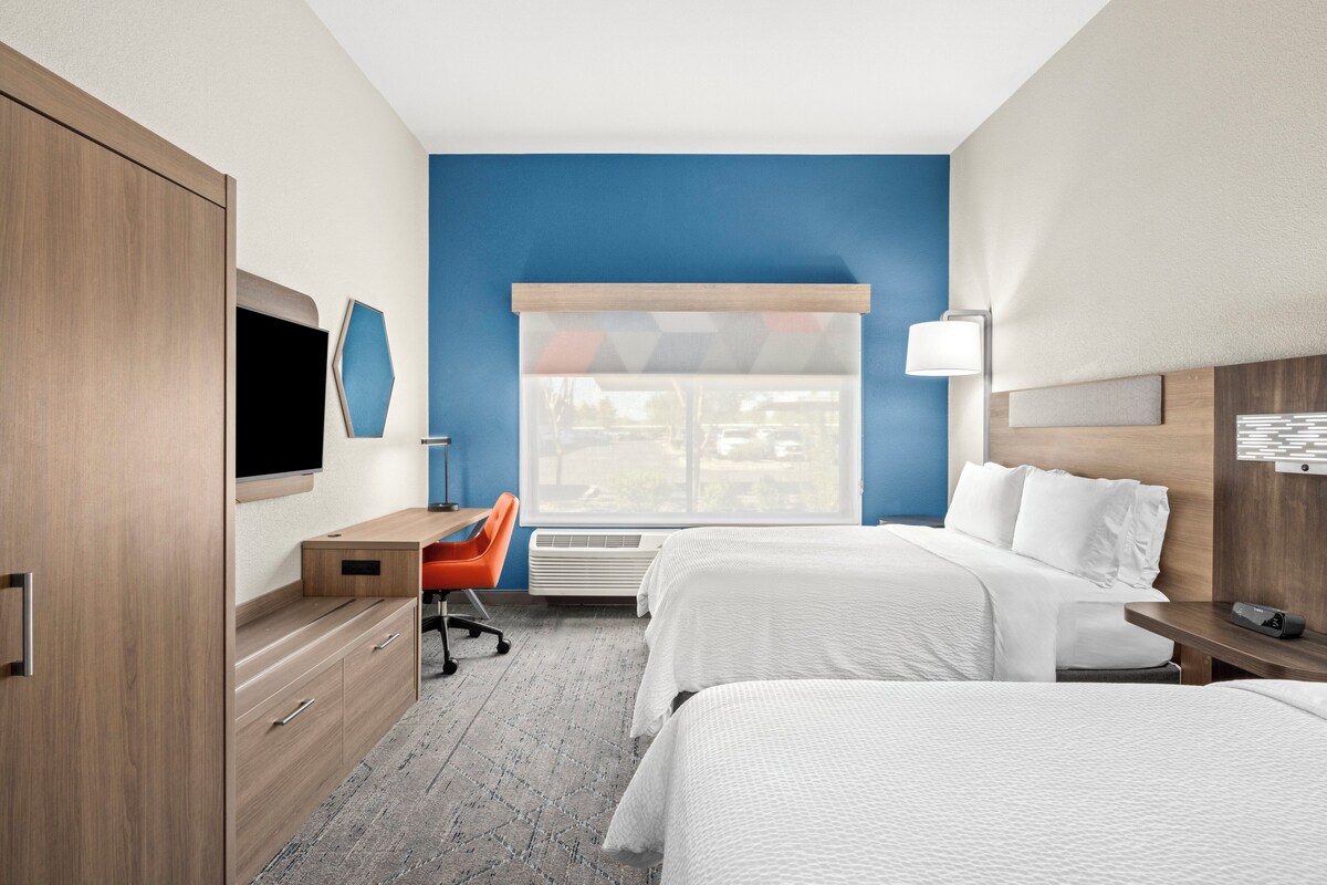 A hotel room with a bed, a desk, a chair, a TV, and a window with blinds.