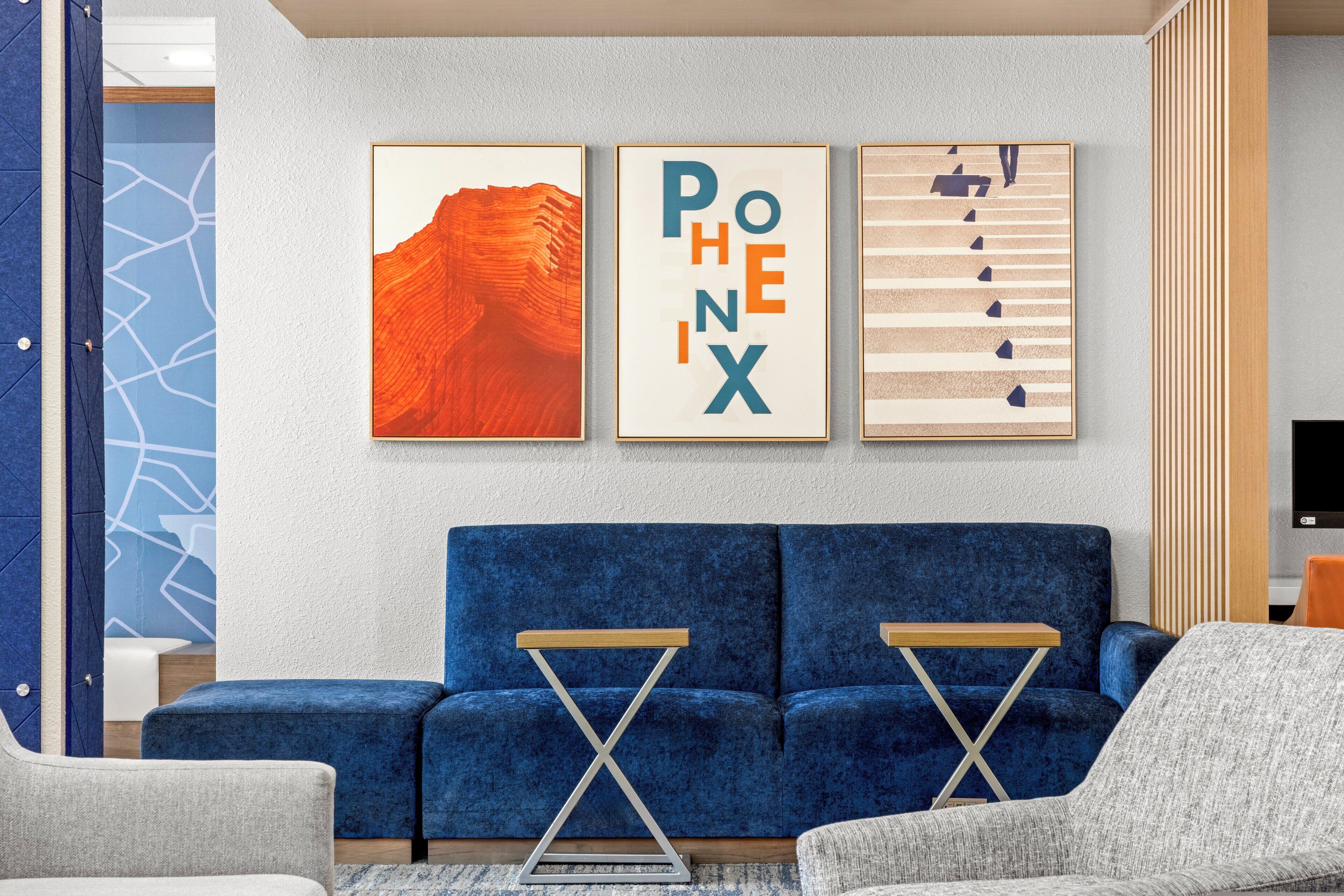 A modern living room with a blue sofa, two wooden side tables, and three framed artworks on the wall.
