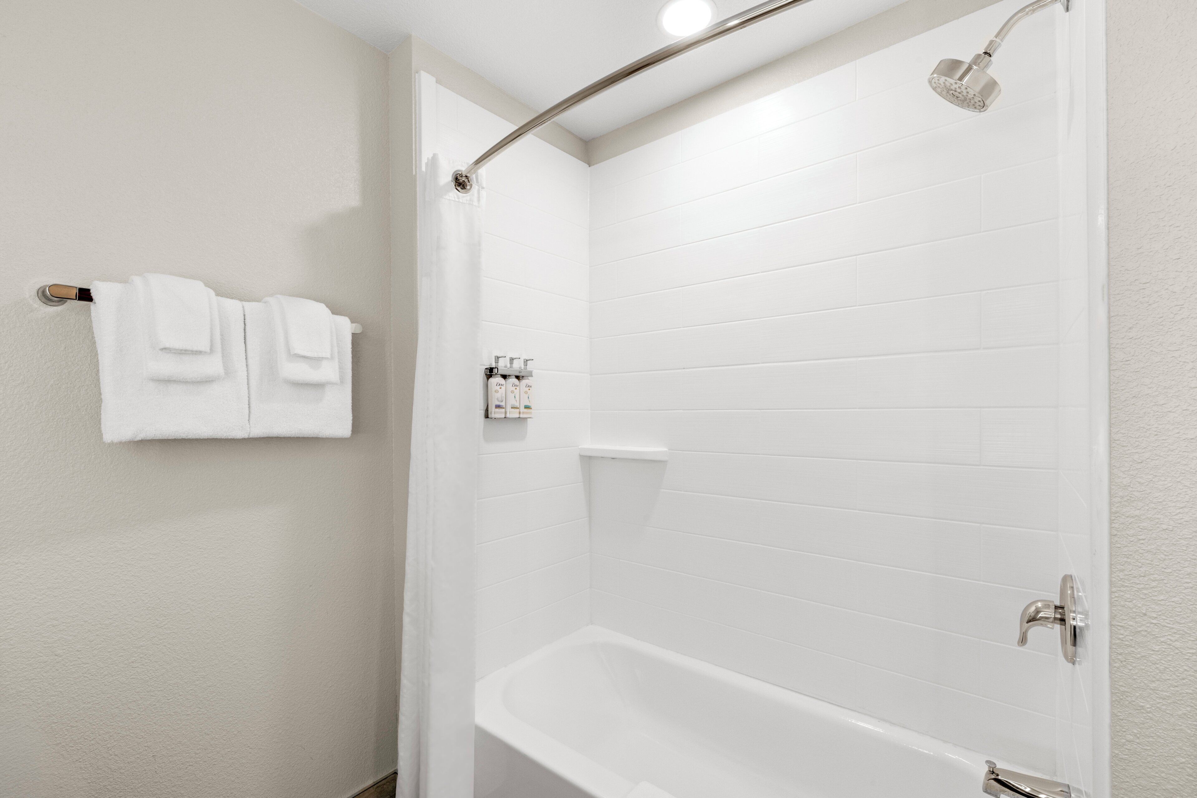Un baño con una bañera blanca, un cabezal de ducha y un perchero con toallas dobladas.