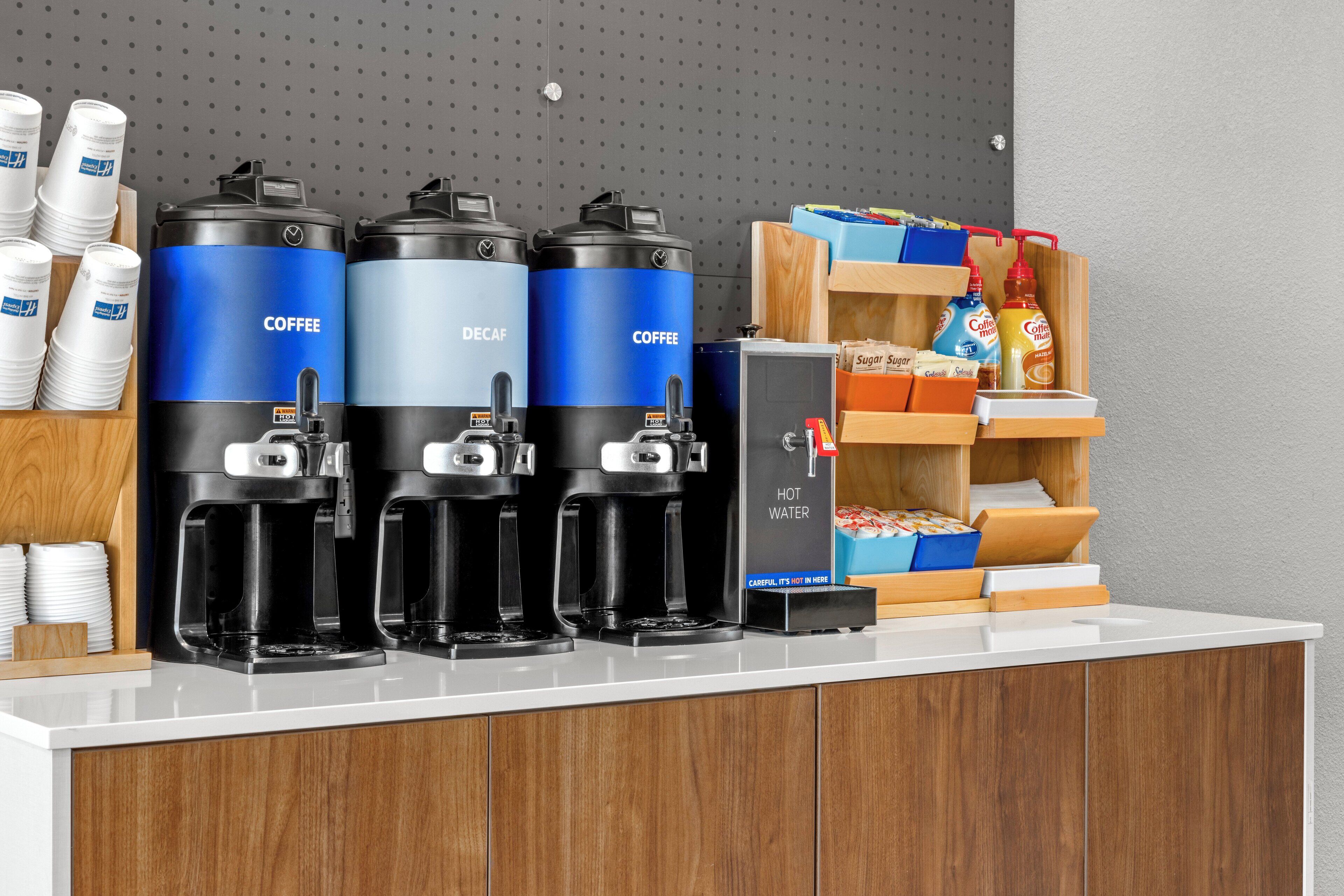 En kaffestation med tre kaffemaskiner, en varmtvandsdispenser samt en dispenser til sukker og fløde.