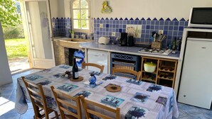 A kitchen with a dining table set for four, a sink, a stove, and a refrigerator. - Stone house with beautiful swimming pool and enchanting panorama (Seguret)