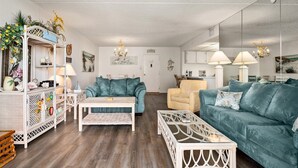Una sala de estar con un sofá color turquesa, una mesa de centro blanca y un mueble de madera con adornos.