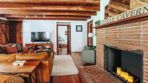 Ein gemütliches Wohnzimmer mit Kamin, Holzbalken, einem Ledersofa und einem Fernseher.
