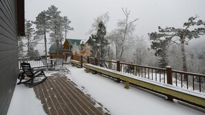 Een sneeuwbedekte veranda met een reling, een schommelstoel en een kleine tafel.