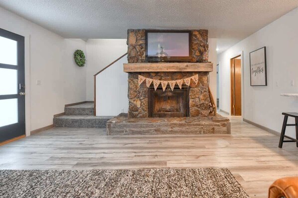Una sala de estar moderna con chimenea de piedra, un televisor encima y una escalera que sube a otro nivel.