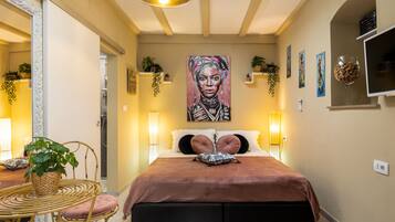 A bedroom with a large bed, bedside lamps, a wall-mounted TV, and a painting.