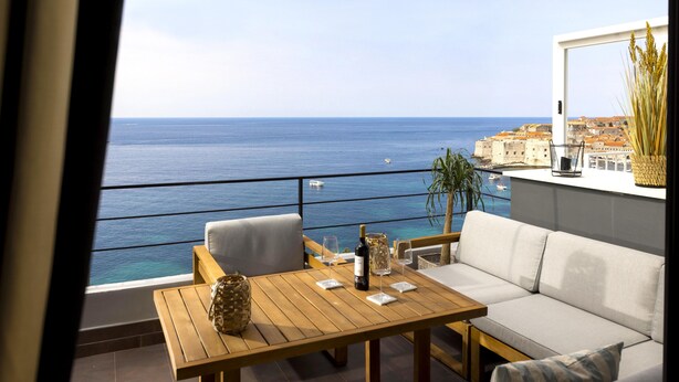 A balcony with a wooden table and chairs, a sofa, and a view of the sea and buildings. - Dubrovnik Old Town Apartments (Dubrovnik)