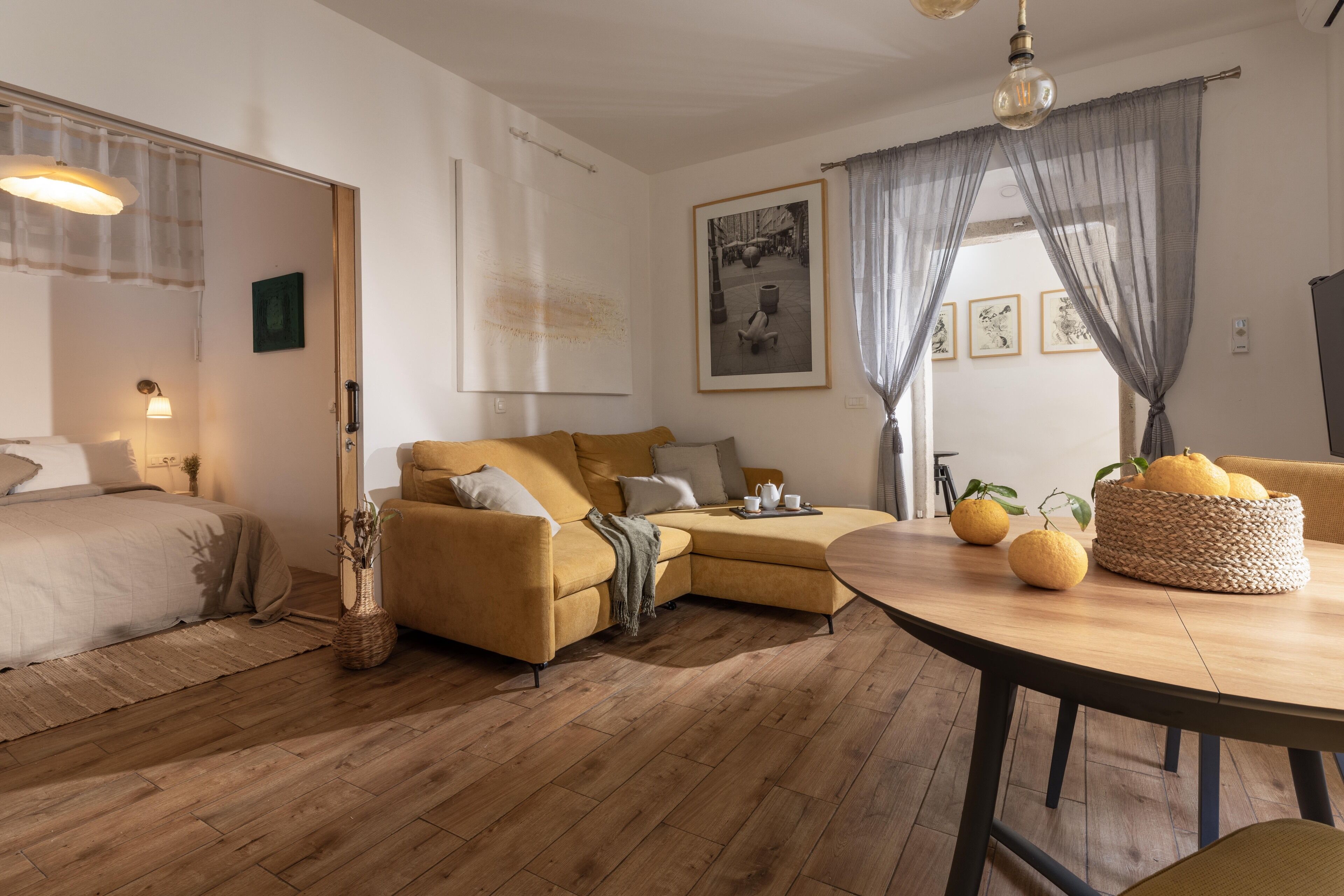 Un salon chaleureux avec un canapé, une table à manger décorée de citrons et une grande fenêtre ornée de rideaux légers.