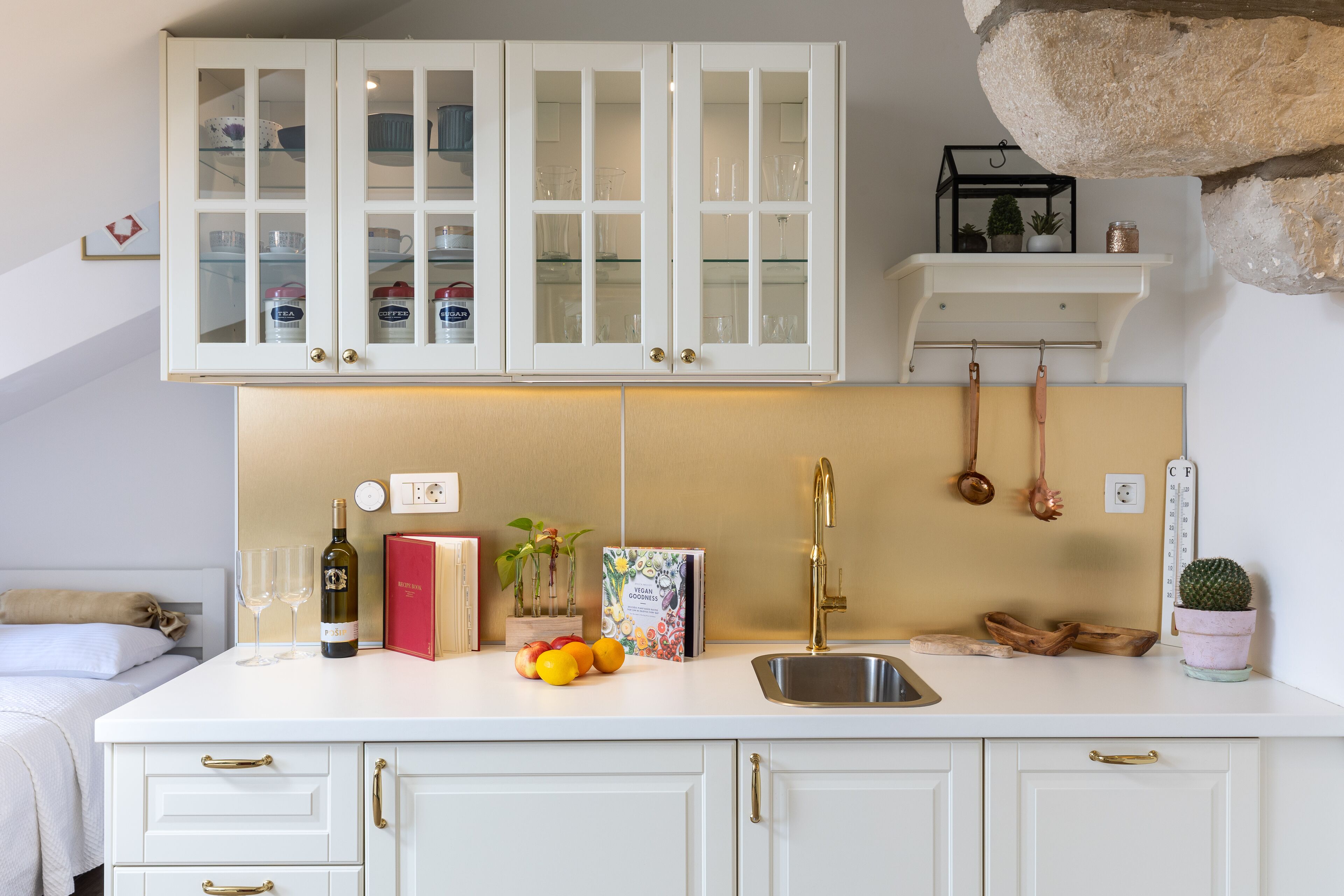 Una cocina con armarios blancos, un lavabo y una encimera con una botella de vino, vasos y frutas.