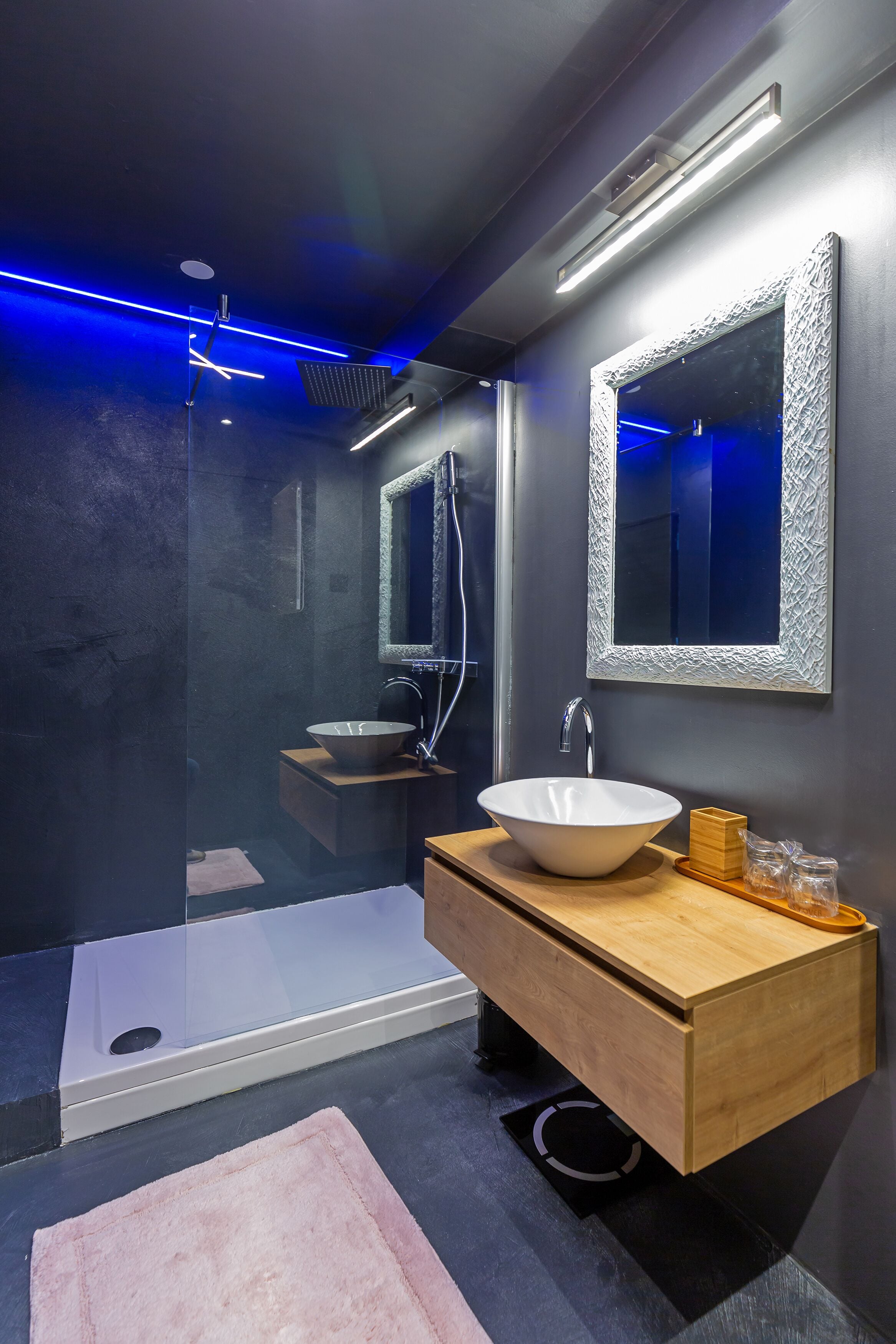 A modern bathroom with a glass-enclosed shower, a wooden vanity with a white sink, and a large mirror with a textured frame.