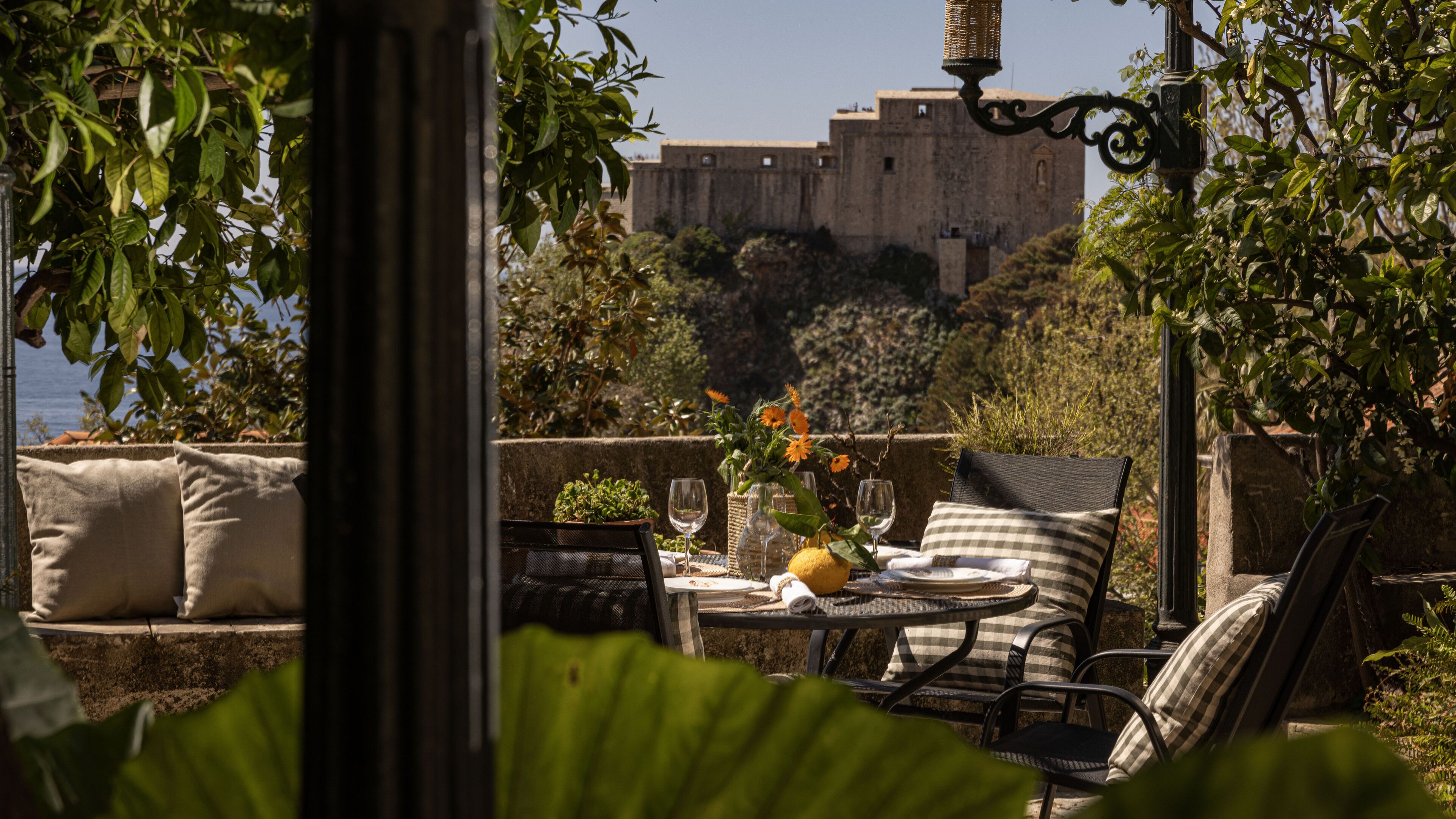 A terrace with outdoor seating, a table with a vase of flowers, and a view of a historic building in the background.