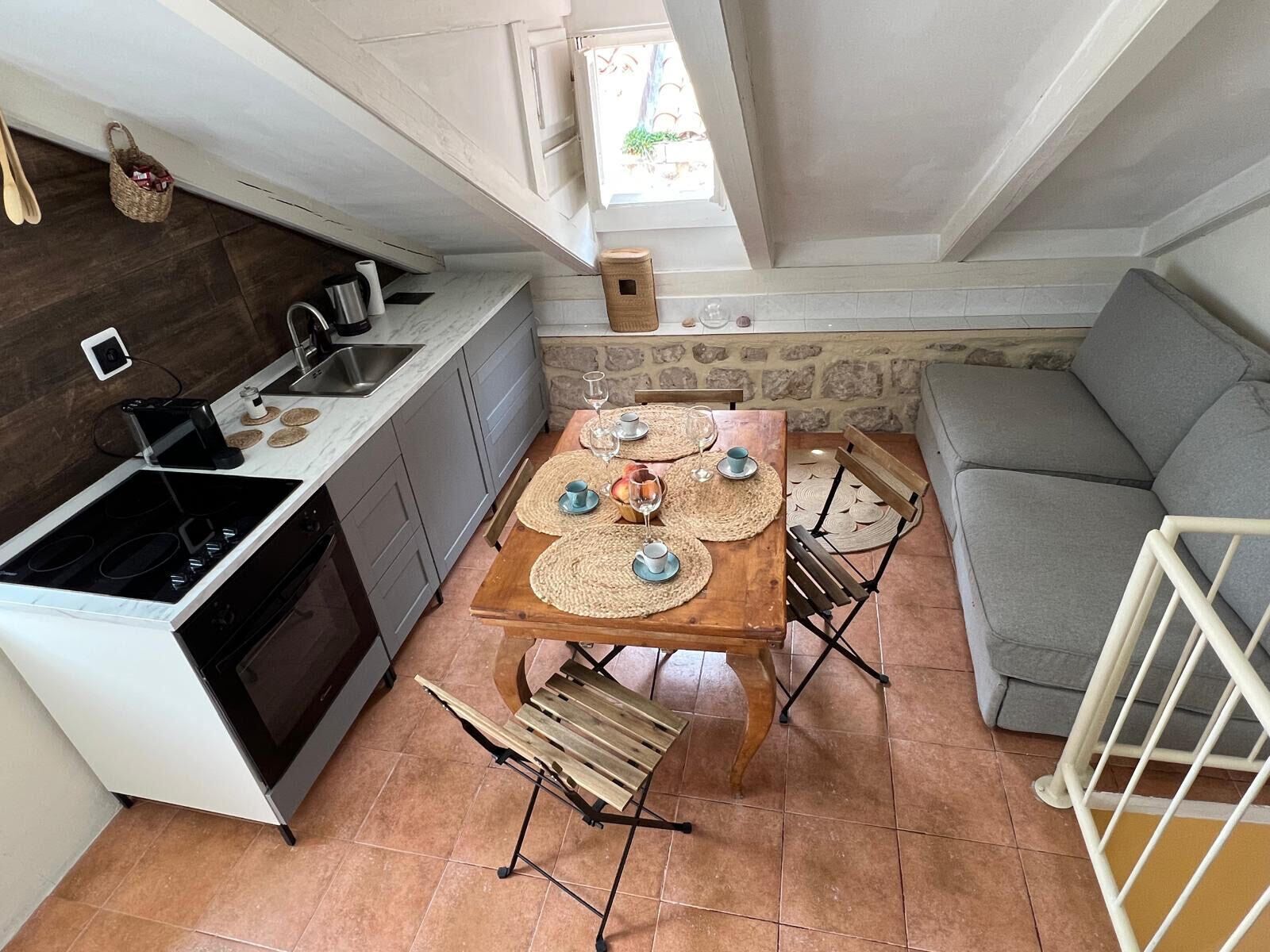 A compact kitchen with a dining area, a stone wall, and a grey sofa.