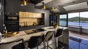 A modern kitchen with a large island, bar stools, and a view of the sea. - Dubrovnik Old Town Apartments (Dubrovnik)