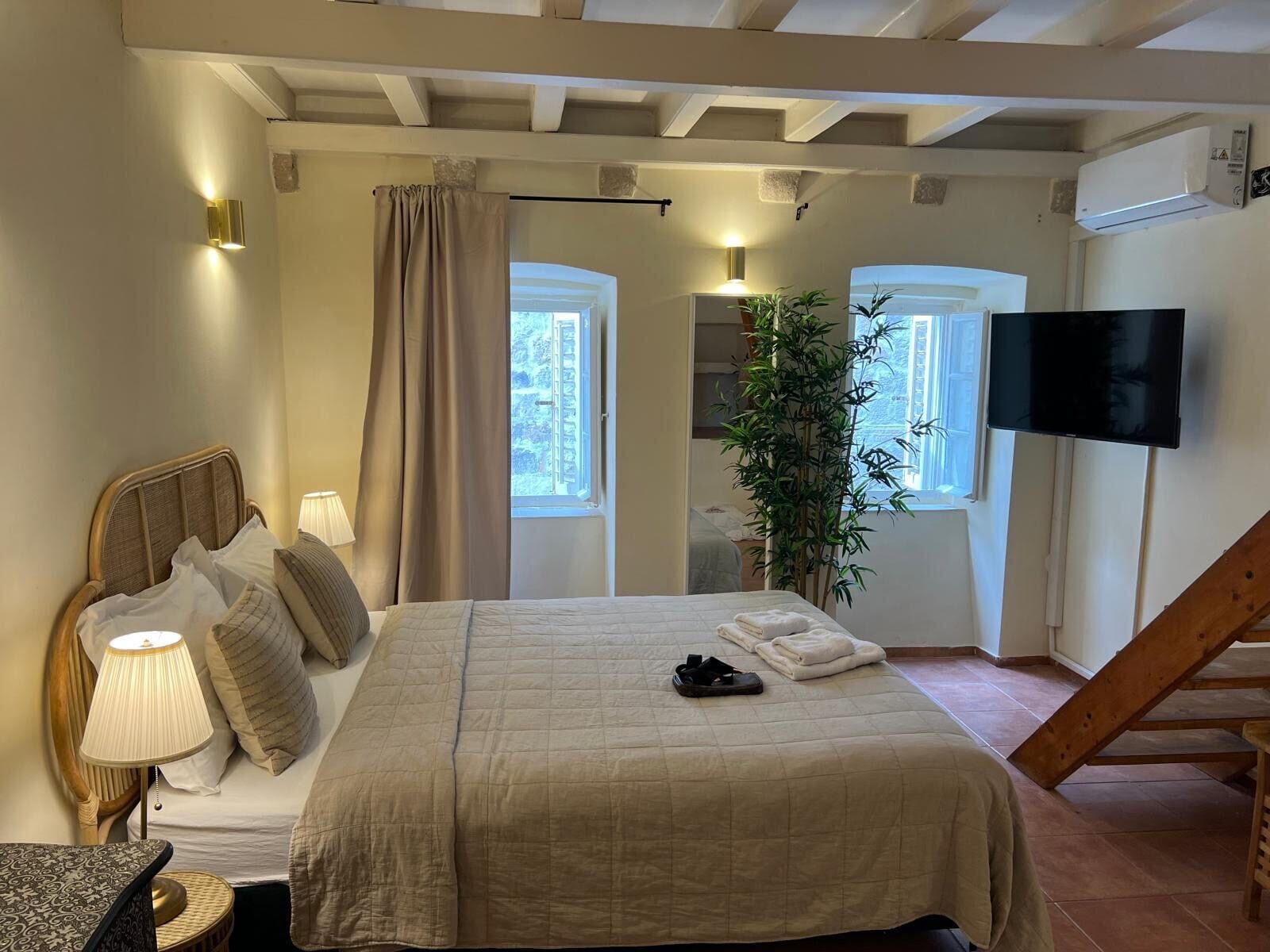 A bedroom with a bed, bedside lamps, a TV, a plant, and a staircase.