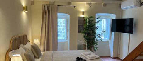 A bedroom with a bed, bedside lamps, a TV, a plant, and a staircase.