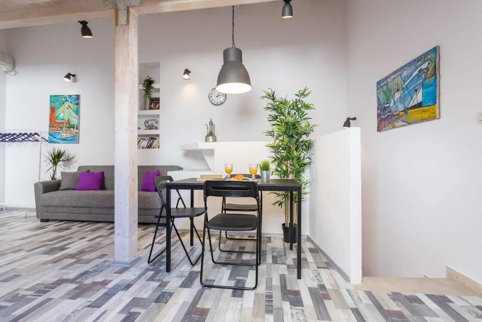 Un salon moderne avec un canapé gris, des chaises noires, une table à manger et une suspension.