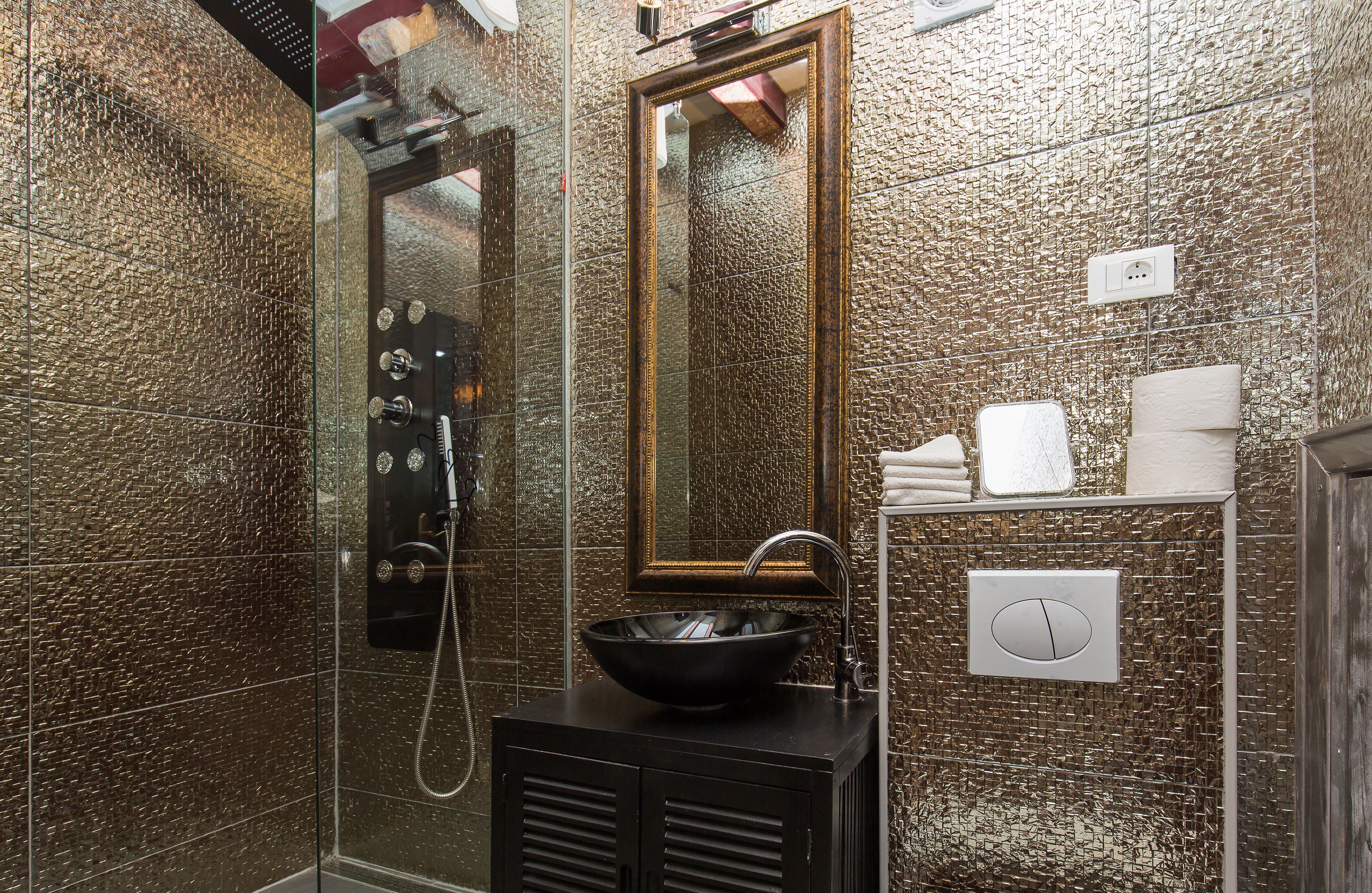 A bathroom with a textured wall, a large mirror, a sink with a black basin, and a shower enclosure.