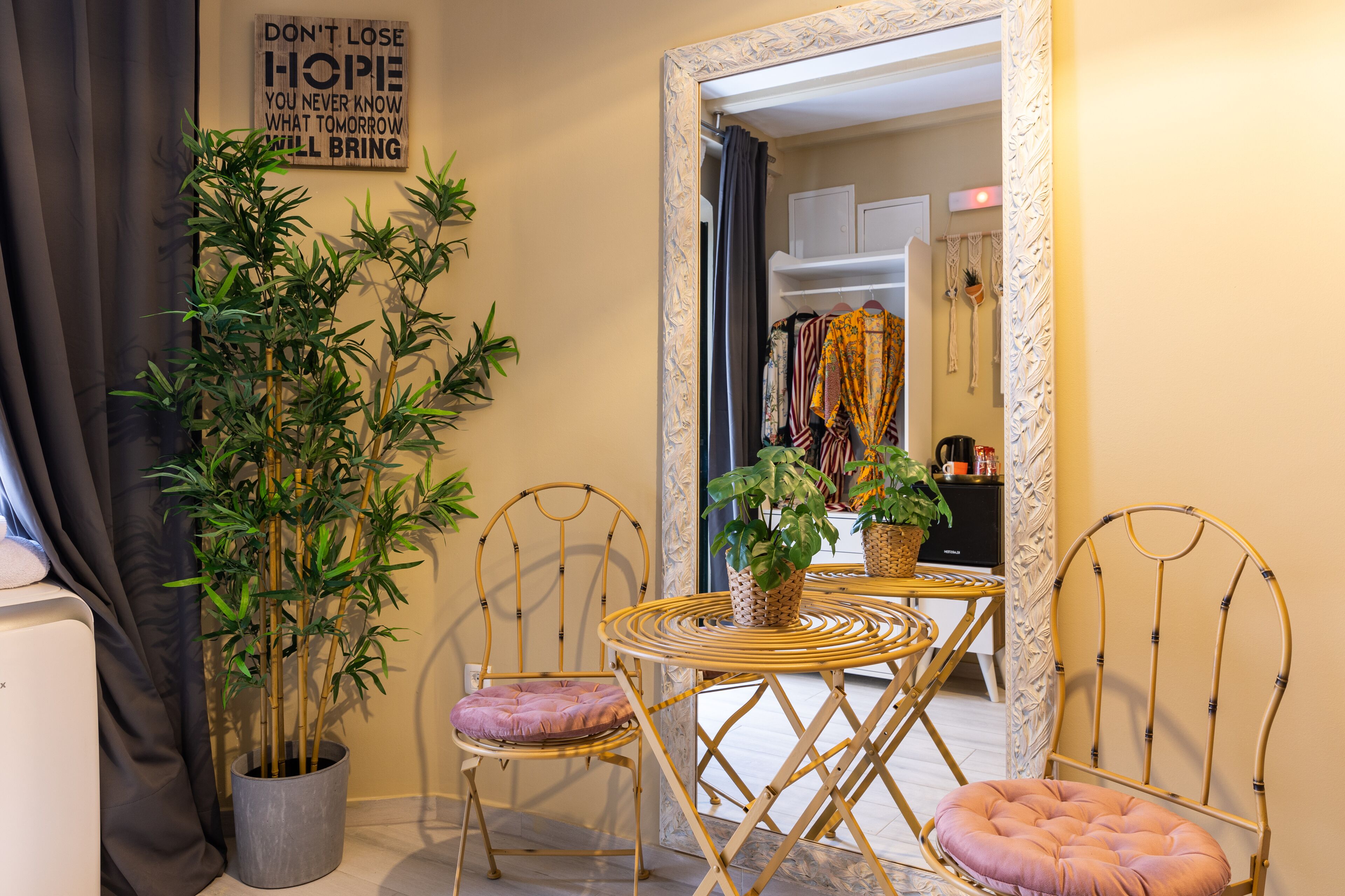A room with a mirror, two chairs with cushions, a small table, and a potted plant.