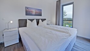 Una moderna camera d'albergo con un letto grande, un comodino con una lampada, e una finestra che si affaccia sull'esterno.