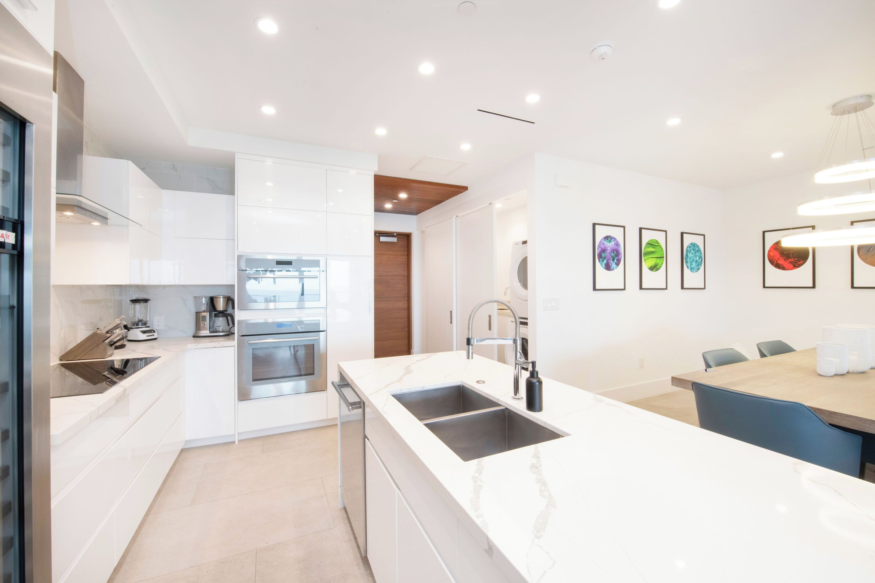 A modern kitchen with white cabinetry, a double sink, and a dining area with a wooden table and chairs.