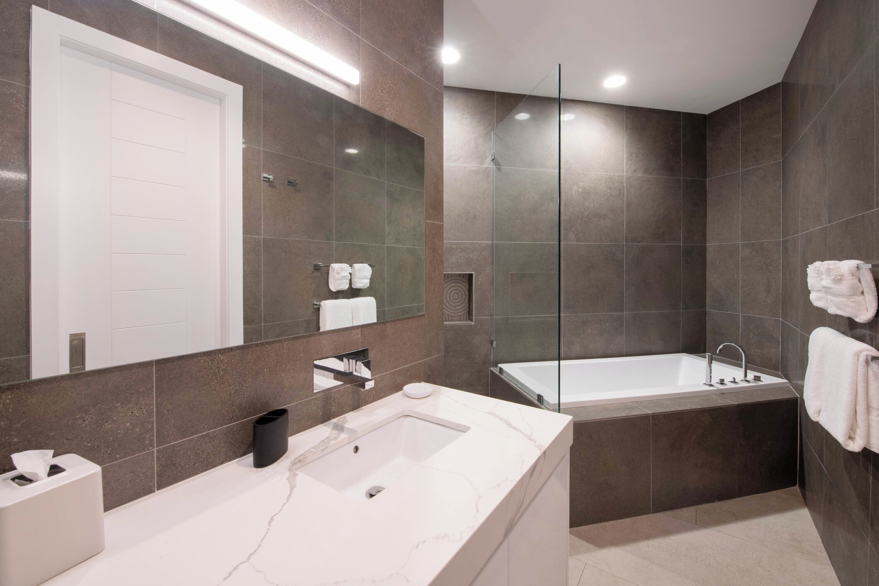 A modern bathroom with a large mirror, a bathtub, and a sink.