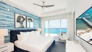 A modern hotel room with a large bed, a desk, and a view of the ocean. - Rum Point Resort 401 by Grand Cayman Villas (Grand Cayman)