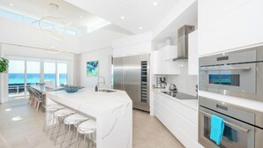 Een moderne keuken met een groot eiland, roestvrijstalen apparatuur en uitzicht op de oceaan.