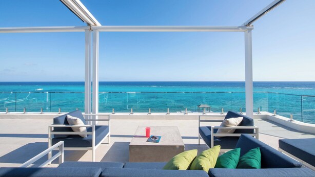 Een balkon met uitzicht op de oceaan, met een bank, een tafel en een glazen hekwerk.