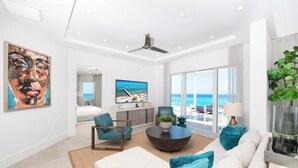 Een moderne woonkamer met een grote televisie, comfortabele zitplaatsen en uitzicht op de oceaan.