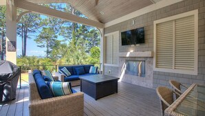 Une terrasse extérieure aménagée avec un canapé, des fauteuils, une table, un barbecue et un téléviseur fixé au mur.
