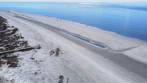 Une plage avec une longue étendue de sable, un petit plan d’eau et un navire au loin.