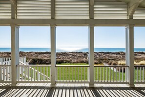 Une terrasse en bois, dotée de rampes blanches, qui offre une vue sur une plage et des dunes herbeuses.