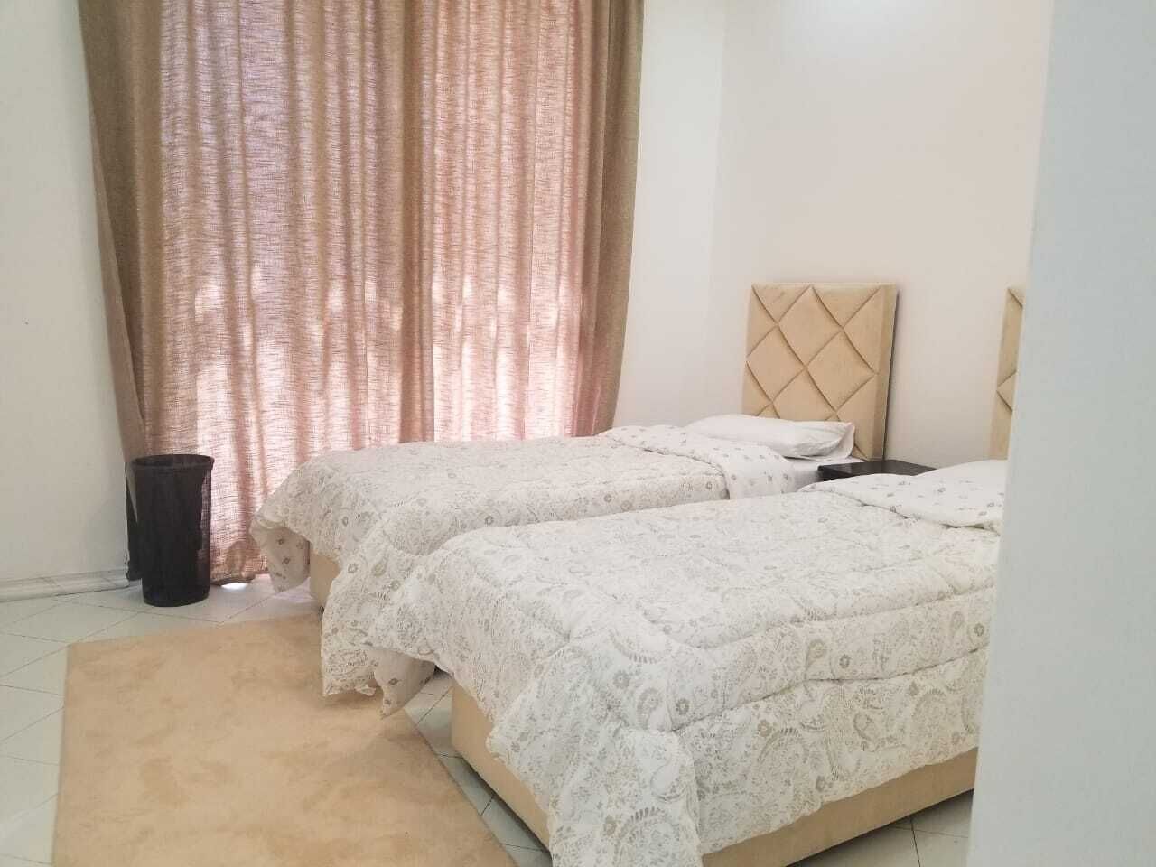 Une chambre à coucher avec deux lits, une tête de lit et une fenêtre avec des rideaux.