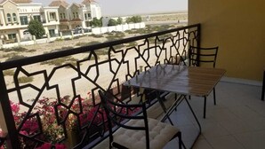 Ein Balkon mit Tisch und Stühlen, Blick auf eine Sandfläche mit Gebäuden im Hintergrund.