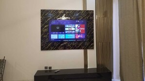 Ein modernes Wohnzimmer mit einem an der Wand befestigten Flachbildfernseher, der Streamingdienste anzeigt, einer schlanken schwarzen Unterhaltungseinrichtung darunter und einer vertikalen Wandverkleidung.