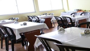 A dining area with tables covered in white tablecloths, black chairs, and a coffee machine in the background. - Tibiriçá Hotel LTDA (Maraba)
