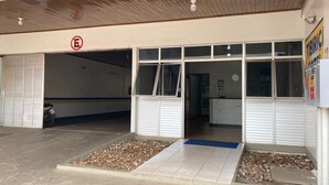 A building entrance with a closed garage door, a no parking sign, and a reception area with a clock. - Tibiriçá Hotel LTDA (Maraba)